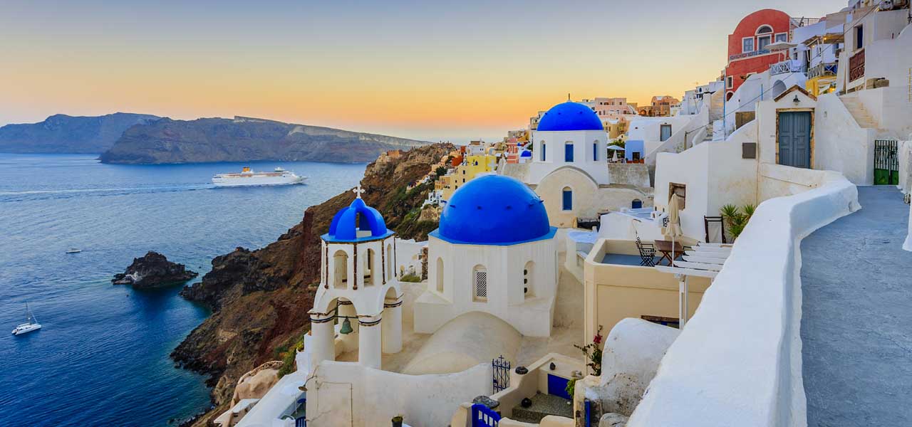 Image of an iconic Greek island hillside town with cruise ship passing in the background